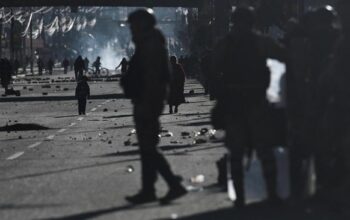 Seorang polisi militer berjalan melewati jalan yang dipenuhi bebatuan berserakan, sementara seorang anak berdiri di tengah lokasi aksi protes terhadap pemerintahan Presiden Rodrigo Paz di El Alto, Bolivia, Sabtu (16/5/2026). Bentrokan pecah saat aparat berupaya membongkar blokade jalan yang telah melumpuhkan akses menuju La Paz selama hampir dua pekan di tengah krisis ekonomi dan bahan bakar yang berlangsung di negara tersebut. (REUTERS/Claudia Morales)