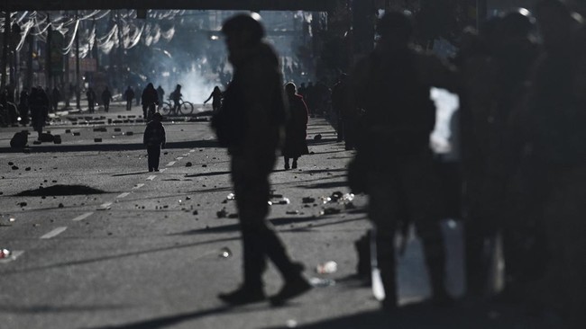 Seorang polisi militer berjalan melewati jalan yang dipenuhi bebatuan berserakan, sementara seorang anak berdiri di tengah lokasi aksi protes terhadap pemerintahan Presiden Rodrigo Paz di El Alto, Bolivia, Sabtu (16/5/2026). Bentrokan pecah saat aparat berupaya membongkar blokade jalan yang telah melumpuhkan akses menuju La Paz selama hampir dua pekan di tengah krisis ekonomi dan bahan bakar yang berlangsung di negara tersebut. (REUTERS/Claudia Morales)