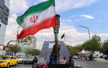 Seorang pria berdiri membawa bendera Iran di persimpangan Valiasr Square di Teheran, Senin (6/4/2026).(AFP/ATTA KENARE)