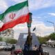 Seorang pria berdiri membawa bendera Iran di persimpangan Valiasr Square di Teheran, Senin (6/4/2026).(AFP/ATTA KENARE)