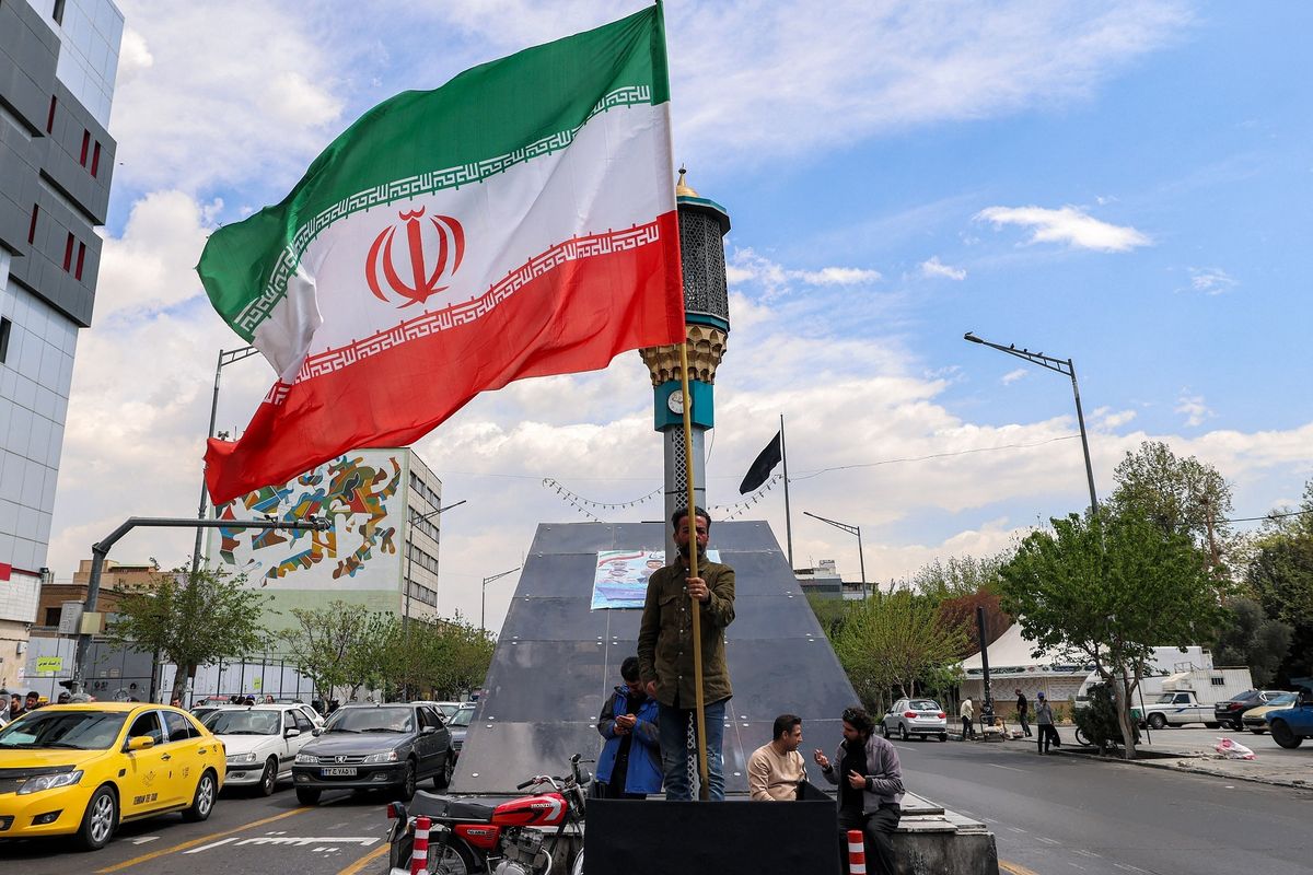 Seorang pria berdiri membawa bendera Iran di persimpangan Valiasr Square di Teheran, Senin (6/4/2026).(AFP/ATTA KENARE)